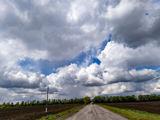 A dirt road in the middle of a field under a cloudy sky