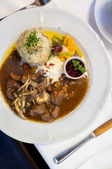 Venison stew with mushrooms, cranberries, horseradish and bread dumpling served on white plate in elegant restaurant