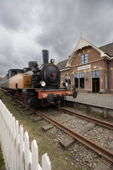 Fototapeta premium Old steam locomotive waiting at Marrum railway station in Netherlands under cloudy sky