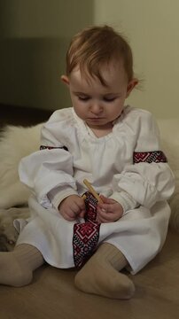 A young child sits on a soft surface, dressed in traditional clothing, engaging with wooden toys. The serene afternoon light creates a warm atmosphere, highlighting the cultural attire.
