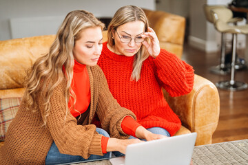 Two women engaged in a serious discussion while working on a laptop at home during a cozy afternoon