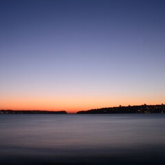 Naklejka premium Serene Sunset over Calm Water and City Skyline
