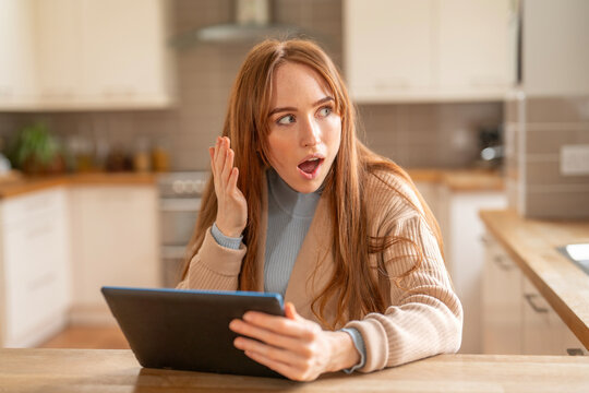 Surprised young woman reacting to something on a tablet in a modern kitchen during the day