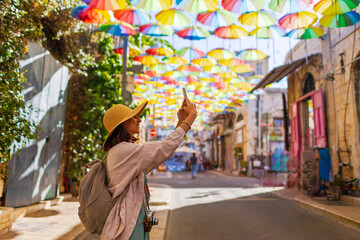 Girl Tourist on an excursion stands on the street with hanging umbrellas and takes pictures. umbrella sky. © zhukovvvlad