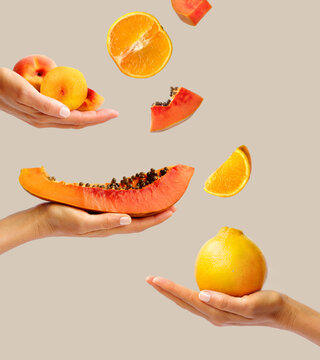 Creative layout made of a hand holding a papaya, orange and peach on the green background. Food concept. Macro concept.