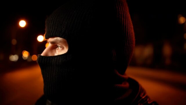 Masked person at night representing anonymity, crime, or social protest