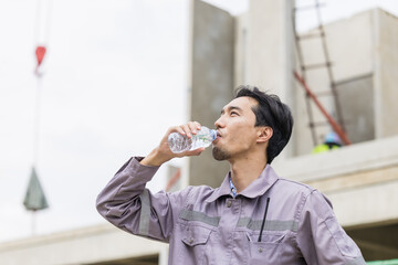Asian worker male thirsty drinking water in hot summer weather working outdoor at construction site