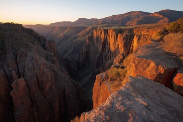 Obraz premium As the sun rises over a gorge, it paints the land with golden hues, creating a breathtaking view of nature's raw beauty and new beginnings.