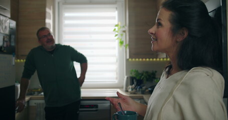Naklejka premium Woman smiling warmly while holding a mug, engaging in a casual conversation with a man standing in the kitchen, fostering a friendly and relaxed atmosphere