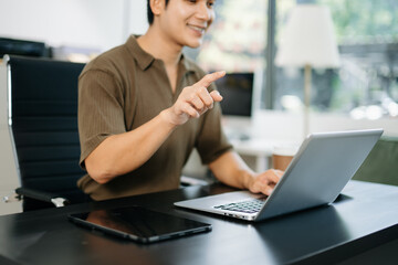 Fototapeta premium Young man typing on laptop and smartphone at modern office desk with coffee and tablet nearby.