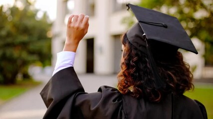 Back view of female student wearing graduation cap and gown, walking outdoors on graduation day - Powered by Adobe