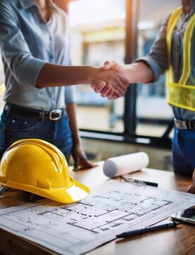 yellow safety helmet on workplace desk with construction worker team hands shaking greeting start up plan new project contract in office center at construction site, partnership and contractor concept