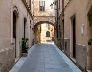 Obraz premium Picturesque alleyway in a historic European town. Sunlit stone buildings, arched passageway, and tranquil atmosphere.