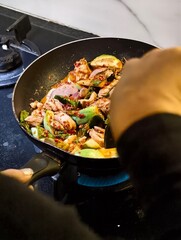 Cooking ingredients in a frying pan, preparing spicy chicken dish on a modern kitchen stovetop