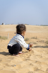 innocent kid trying to hold sand in hand at desert at day from back