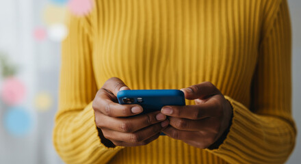 Black woman in yellow sweater using a blue smartphone, blurred background