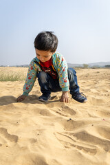 alone rural kid playing in desert sand at bright daylight