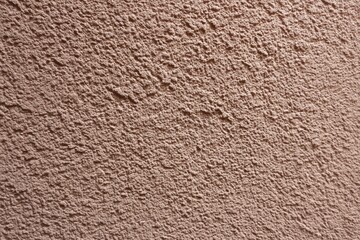 Rough, textured brown wall surface with a grainy, stucco-like finish and natural light casting soft shadows, sustainable building materials
