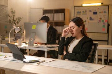A woman is sitting at a desk with a laptop and a computer monitor