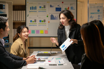 A woman is standing in front of a group of people and holding a piece of paper