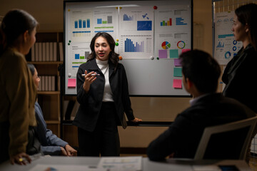 A woman is standing in front of a white board with a group of people around her