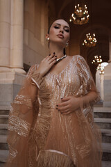 beautiful woman with dark hair in luxurious dress with accessories posing on the stairs of elegant...