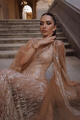 beautiful woman with dark hair in luxurious dress with accessories posing on the stairs of elegant...