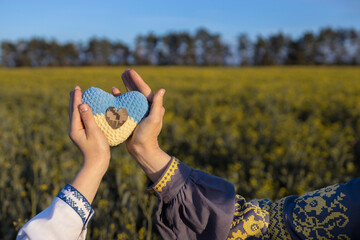 yellow blue knitted heart and camouflage heart on it in hands of child and woman in Ukrainian embroidered shirts. Patriotism. Independence Day. Concept of support and faith in the Armed Forces