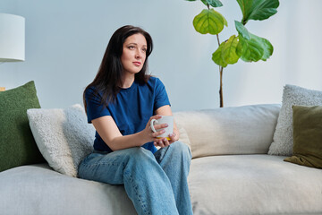 Portrait of beautiful smiling young brunette woman sitting on sofa in living room