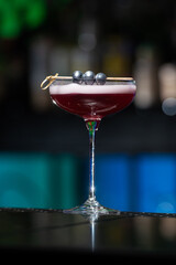 purple cocktail with a foamy white top is garnished with skewered blueberries on a textured bar surface