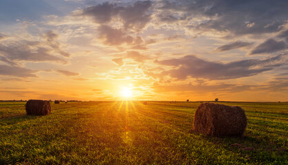 Scenic sunset over hay bales in a field. Golden light bathes the landscape, creating a tranquil scene. For agriculture, travel and inspiring greeting card designs. © Eugene_Photo