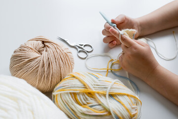 Hands crocheting with yarn balls and scissors on white surface