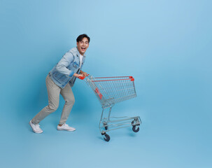 Happy excited Asian teen man pushing empty shopping cart or shopping trolley running promotion...