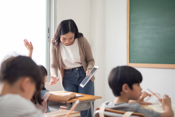 Asian Teacher interacts with students using digital tablet while encouraging participation in a...