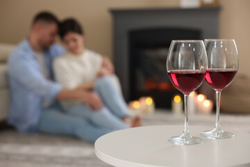 Couple near fireplace at home, focus on glasses of wine