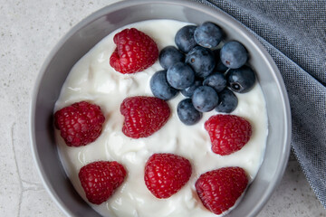 Gray bowl and natural yogurt with berries on the stone marble table.