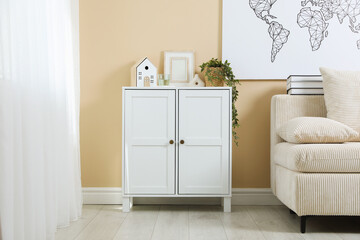 Dresser with stylish decor and houseplant near beige wall indoors