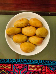 Eight yellow mangoes on a white plate on a table. Tablecloth with an ornament at the bottom. View of tropical fruits