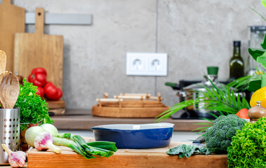 Food background. Healthy eating, cooking and blogging banner. Cutting board with bakicng dish, raw onion, farm vegetables and herbs on cozy kitchen with wooden table, kitchenware and utensils