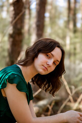 Fototapeta premium Young woman in green dress looking at camera against natural background. Calm and thoughtful look.