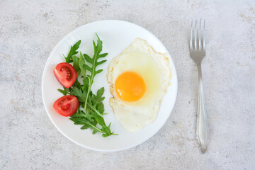Fried Egg with Tomatoes and Arugula on a White Plate with a fork