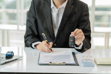 Small car salesman sitting on a table surrounded by calculators and keys while someone is writing something in the background. Car sales concept.