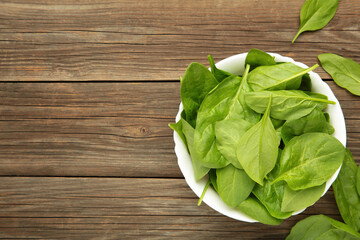 Baby spinach leaves with water drops in mint bowl on grey wooden background. Raw organic spinach greens