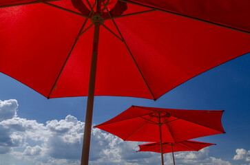 Bright Red Sun Umbrellas Against Blue Sky with Fluffy Clouds on a Hot Sunny Summer Day