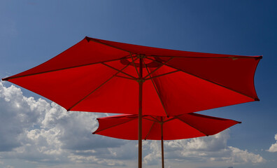 Bright Red Sun Umbrellas Against Blue Sky with Fluffy Clouds on a Hot Sunny Summer Day
