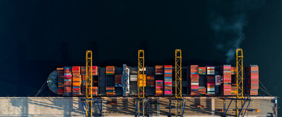 Top view of a large cargo ship loading and unloading containers at a deep-sea port. This aerial scene highlights global logistics, international trade, and maritime transportation hubs.