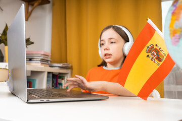 Little girl with laptop and Spain flag. Language courses concept.