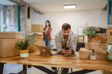 man use mobile phone while woman hold and unpack boxes at new place