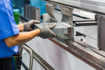 Close up the bending machine operator hold the sheet metal parts with rubber glove.