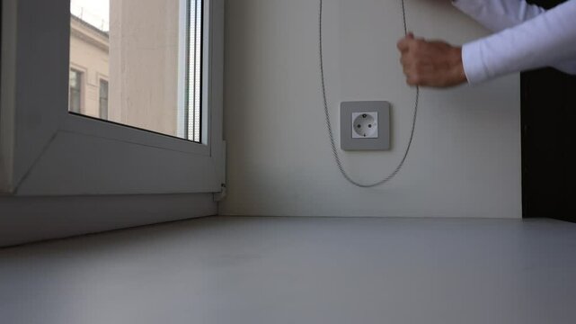 Close-up of womans hands lifting roller blinds on the window in a chain, opening curtains in good day